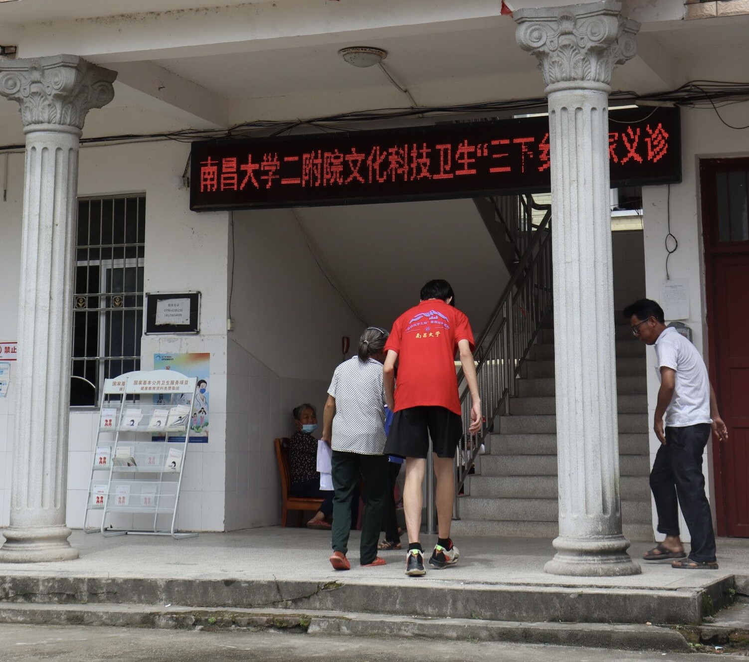 图为实践队员搀扶老人去二楼测量心电图。