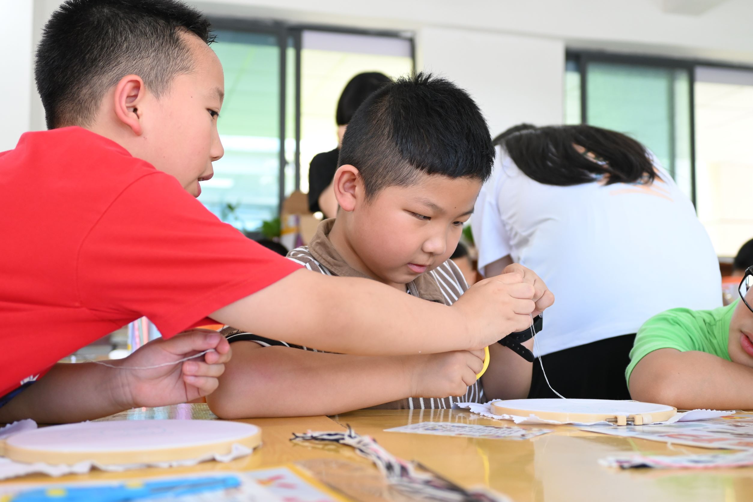 刺繡課上一名學生協助同學進行穿針。