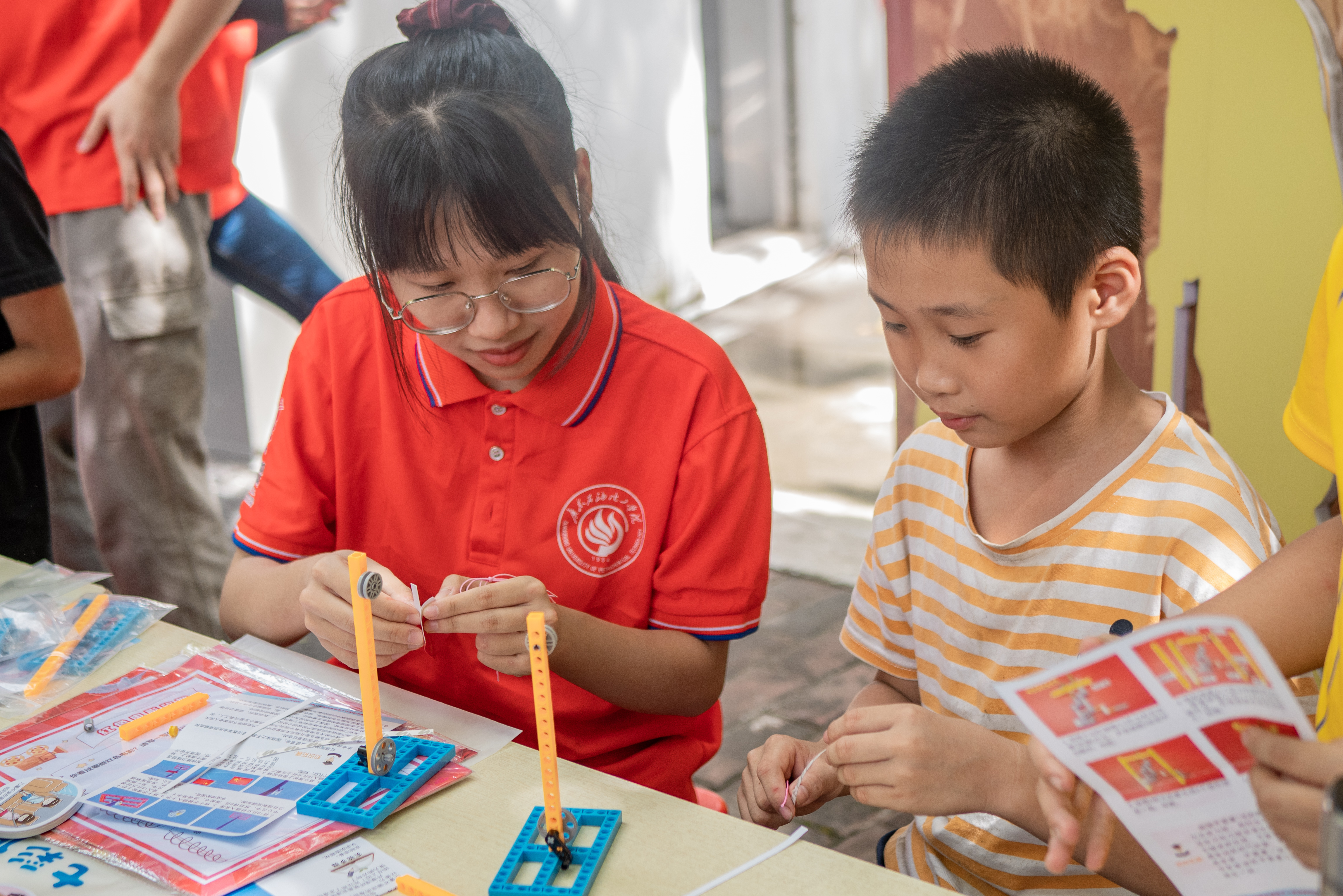 图为广东石油化工学院“绿创使者”志愿服务团队志愿者与孩子们进行组装简易升国旗装置，让他们亲自让小国旗升上去。