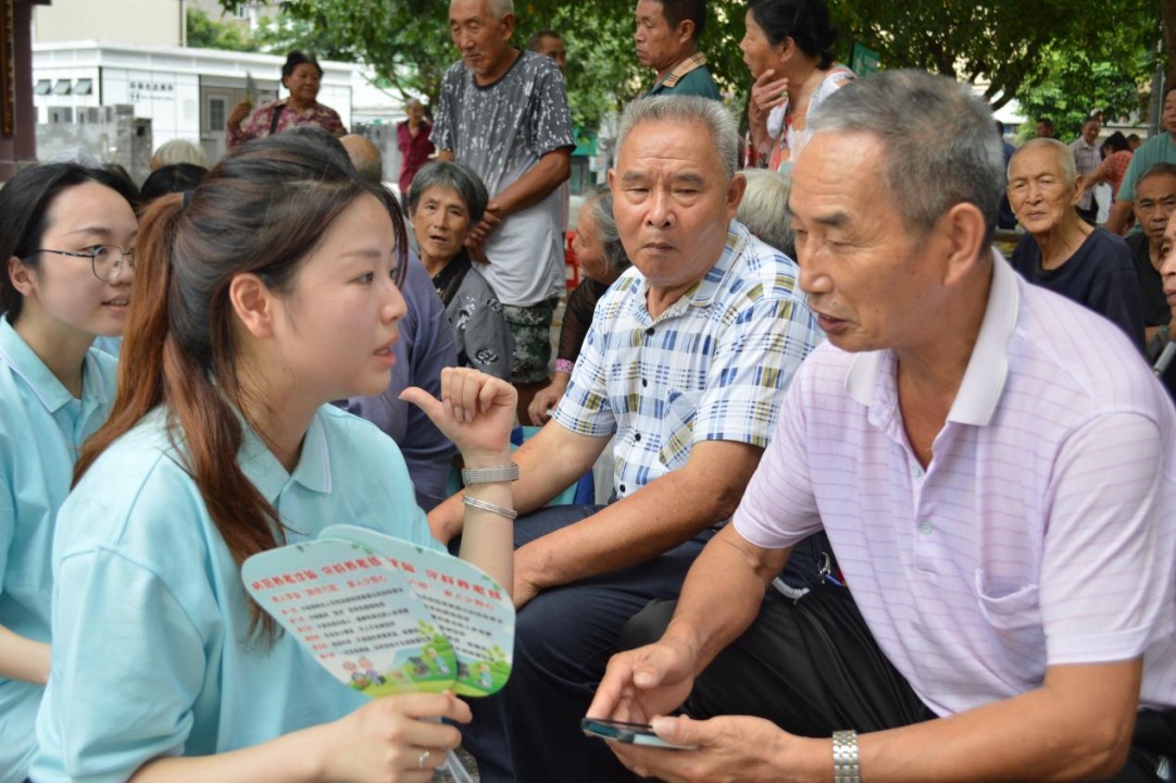 图为实践团成员向居民发放印有防范电信诈骗技巧的扇子。