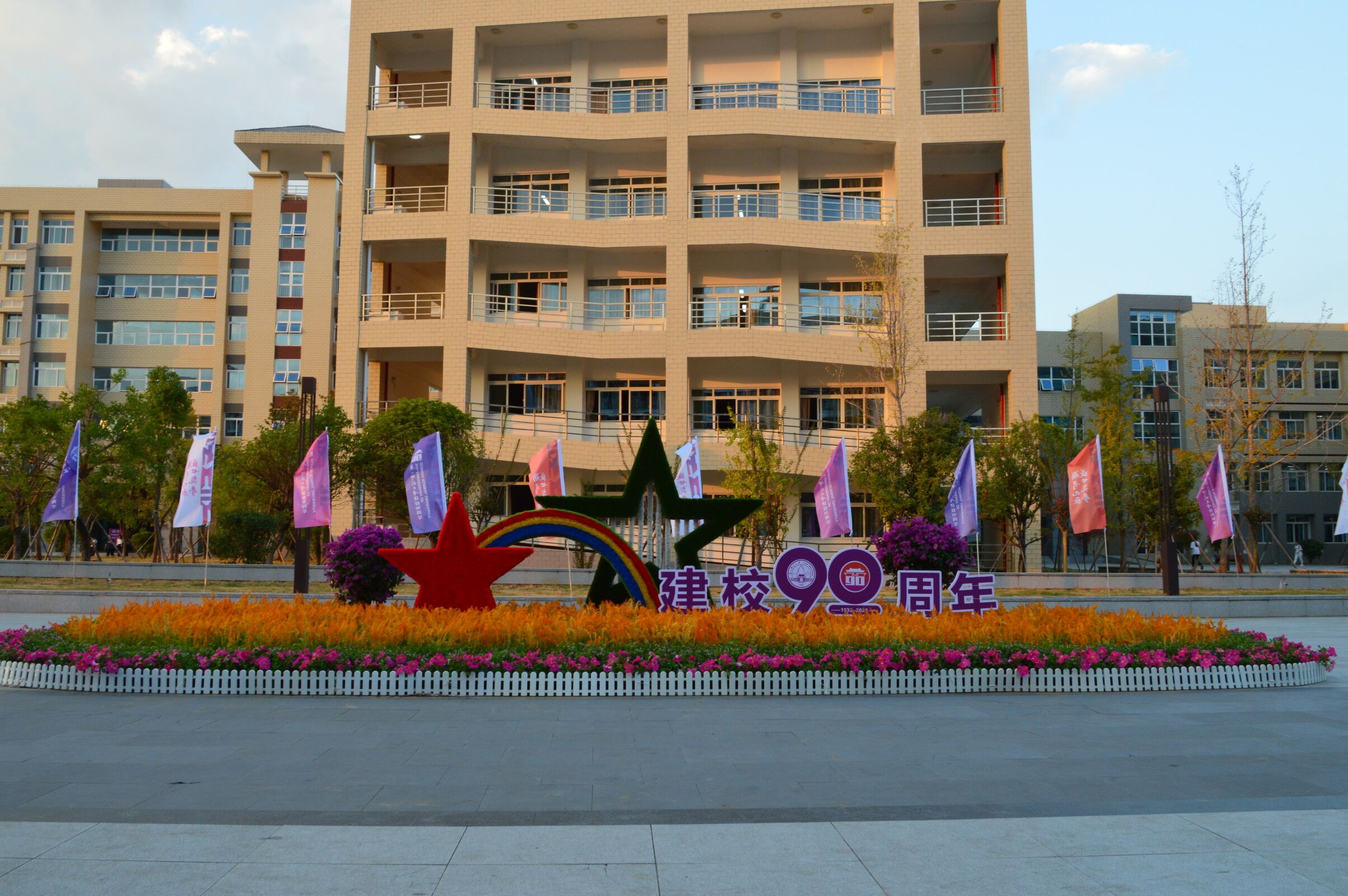 独立小景，亦显风彩。在落日的余晖下，理科楼前彩旗翻飞，“建校90周年”的小景显得格外耀眼。彩虹连接起闪耀的五角星，象征着九十年来师大人薪火相传谱写下的风采华章；绿叶红花与金色的稻穗在微风中共舞，寄予师大未来发展将充满着美好的希望，收获累累硕果。柔和温暖的阳光里，校庆热烈的节日氛围和秋日校园的静谧美好交相辉映。.jpg