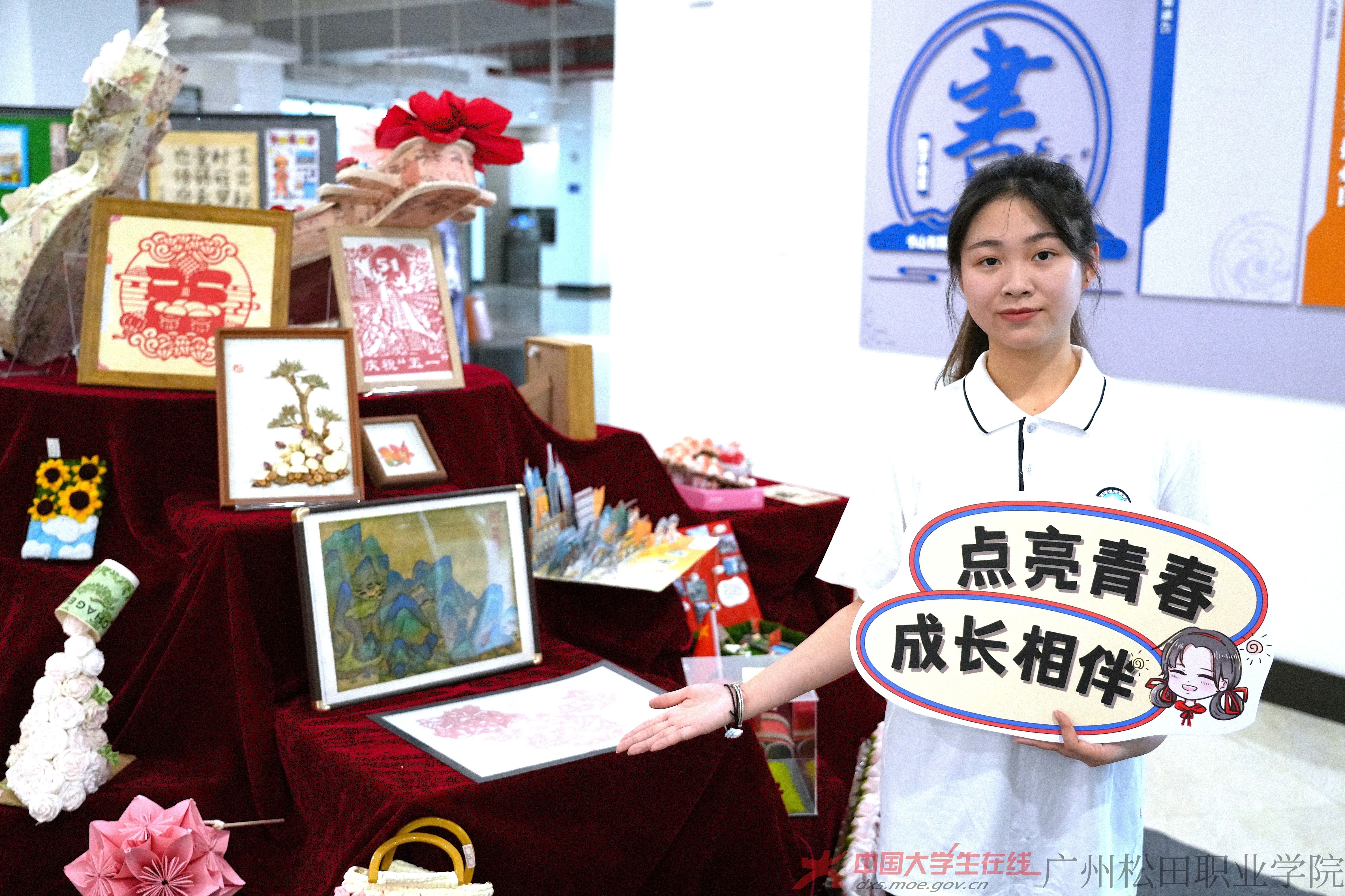 剪紙、繪畫、手工花束等手工藝品錯落有致。謝美紅同學面帶自信微笑，伸手示意身旁佳作，盡顯青春創意與勞動之美。