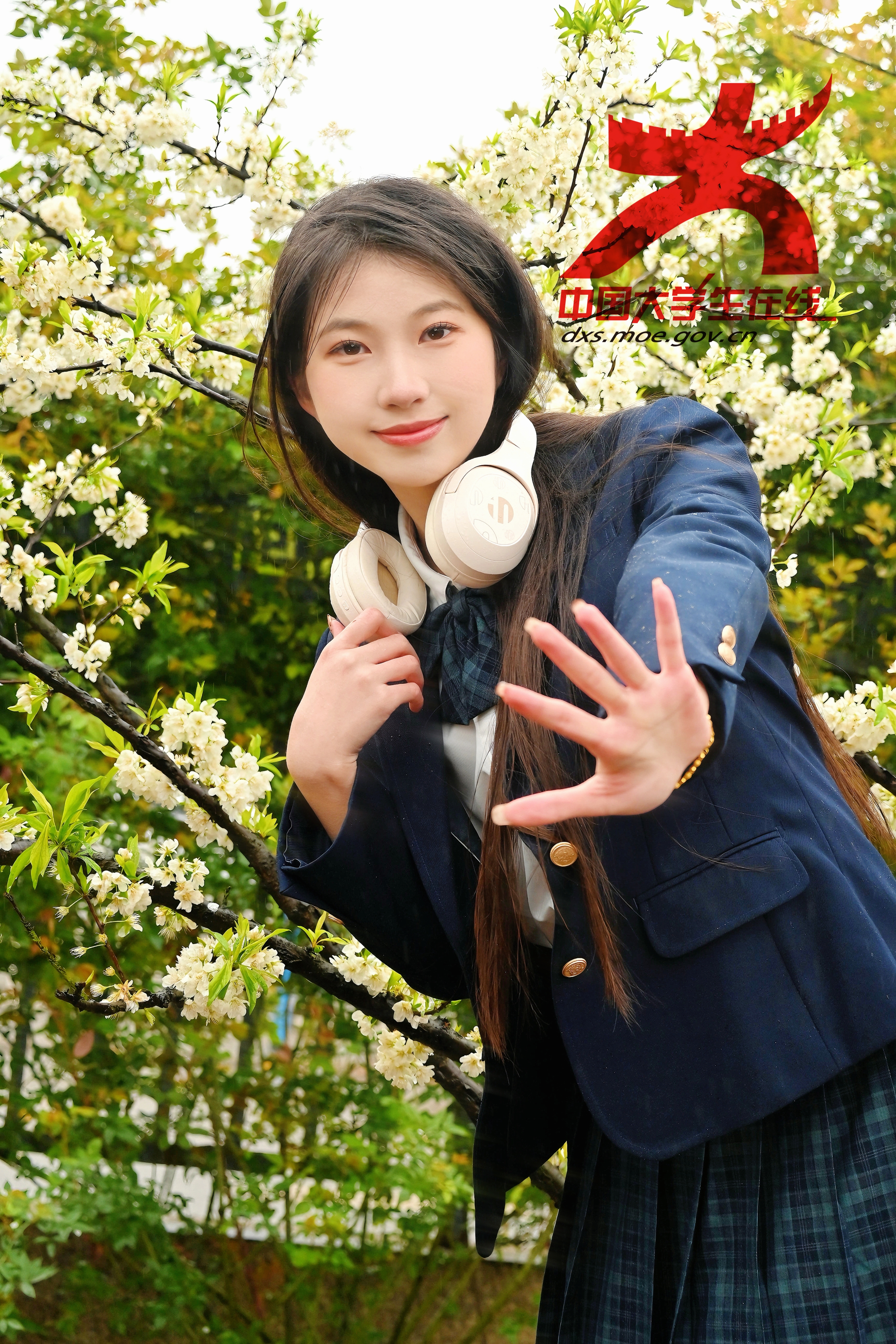 花下邀约：女孩身着清新制服，颈挂白色耳机，站在花下，面带笑容，伸手似在热情邀约，青春气息与烂漫春花相互交融。盛雅婷/摄