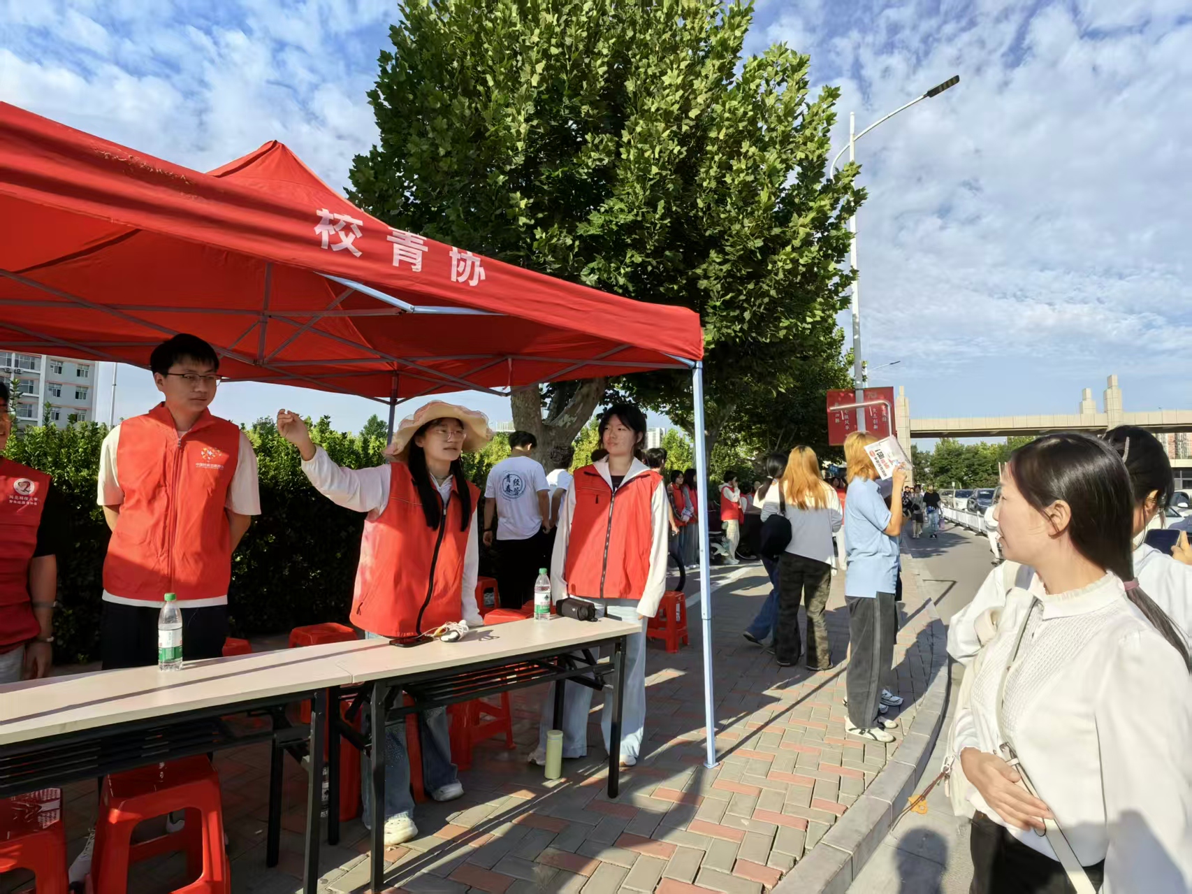 校青协志愿者身着红色志愿马甲，在迎新服务点位值守，热情为入校新生提供引导咨询服务