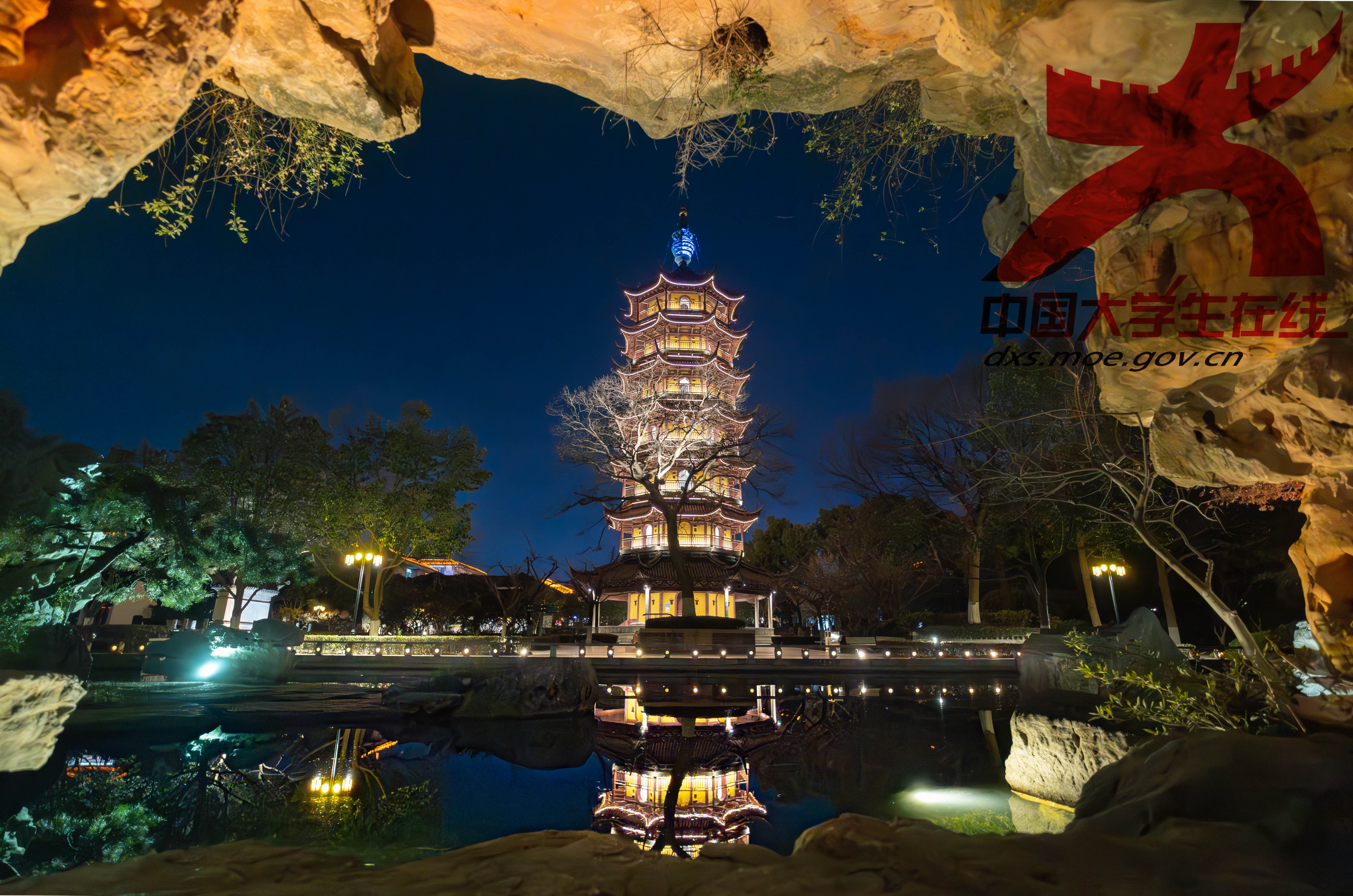 夜下灯塔：当夜幕降临，暖黄色灯光照亮四周。透过石洞望去，塔楼与水中倒影对称，周边绿植点缀。钱烨/摄