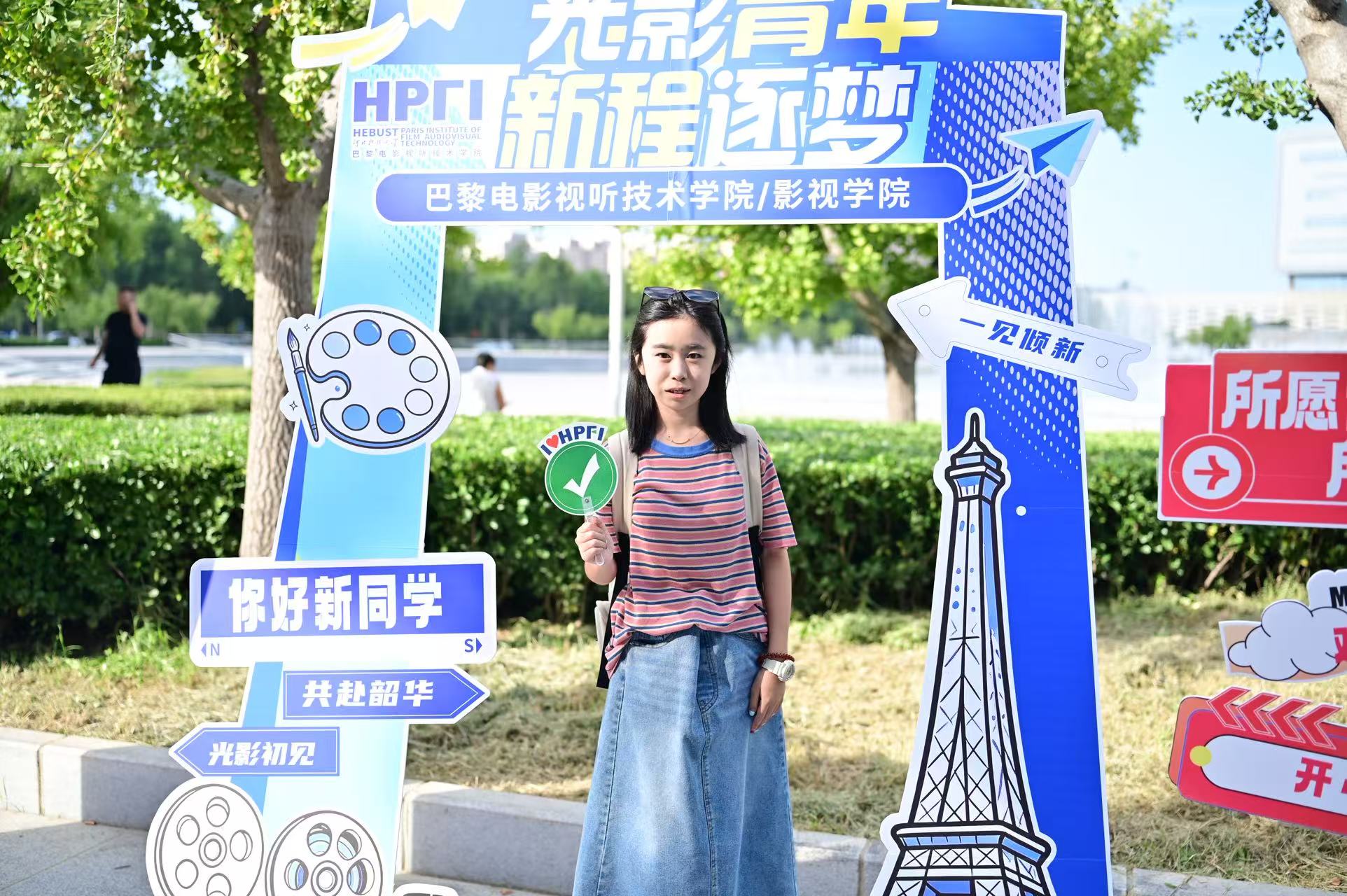 巴黎电影视听技术学院 / 影视学院迎新打卡点，新生手持手举牌，在 “光影青年 新程逐梦” 展板前拍照留影