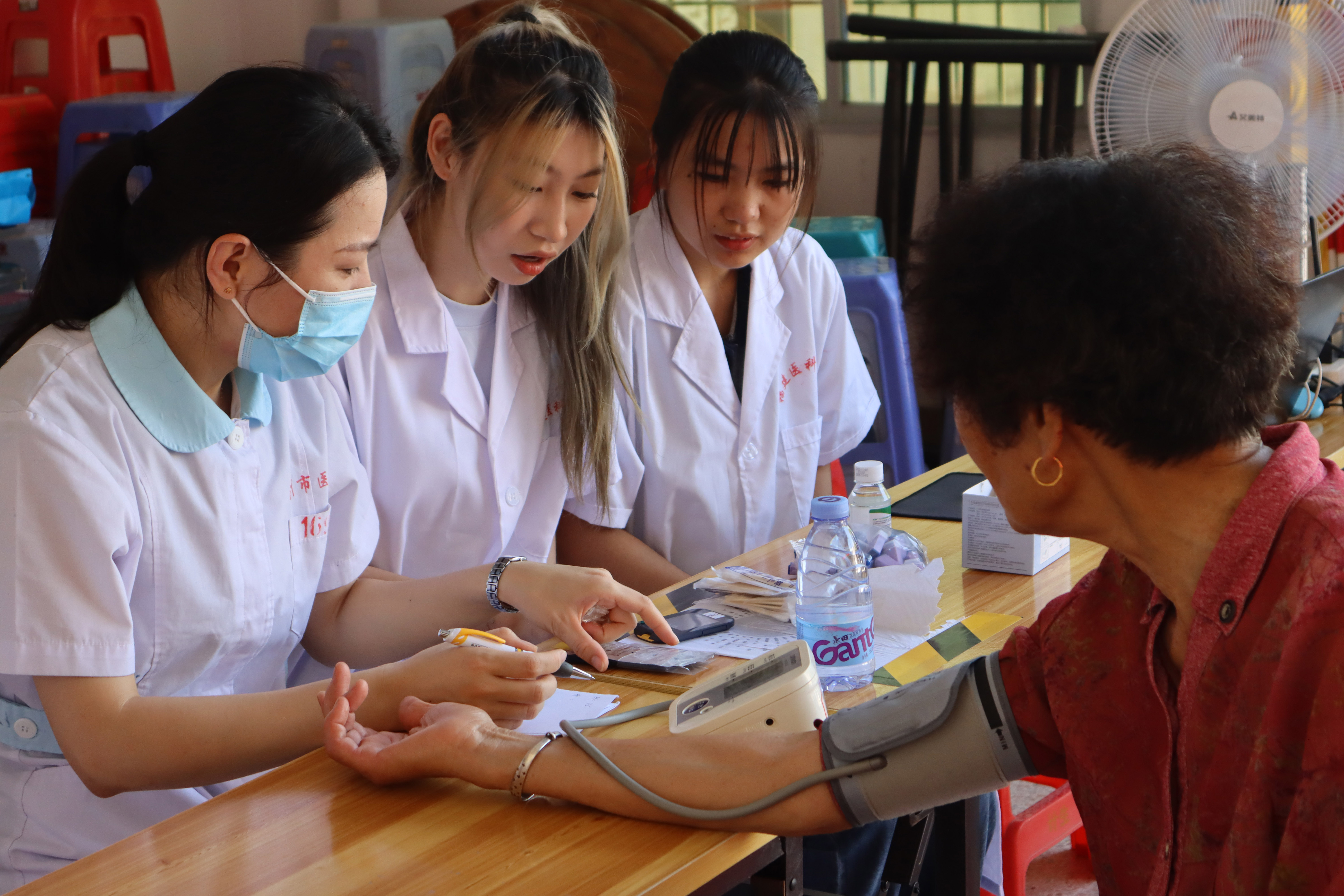 02队员周冰倩、陈昕协助医生为村民测血压。（游钰扬/摄）